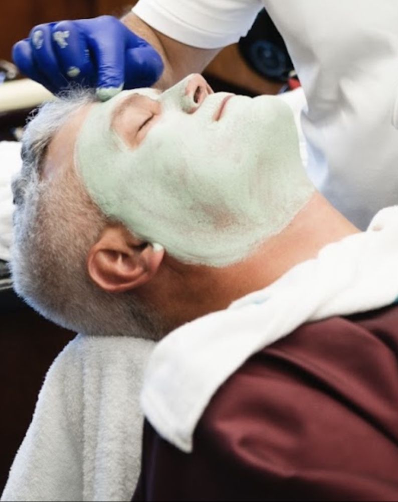 Client relaxing during a men's clay facial treatment with hot towels