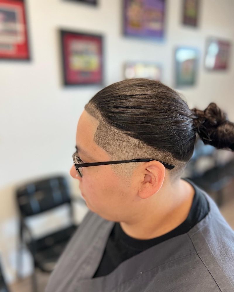 Long hair pulled into a bun with a razor-lined drop fade around the ear