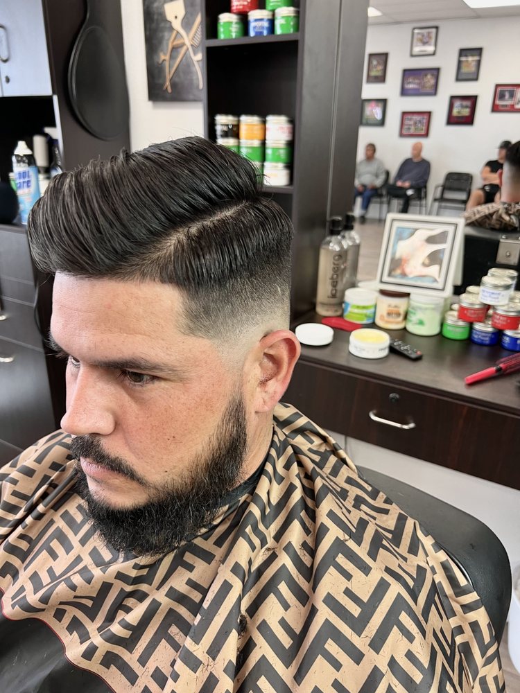 Textured pompadour with a hard part, mid fade and lined-up beard
