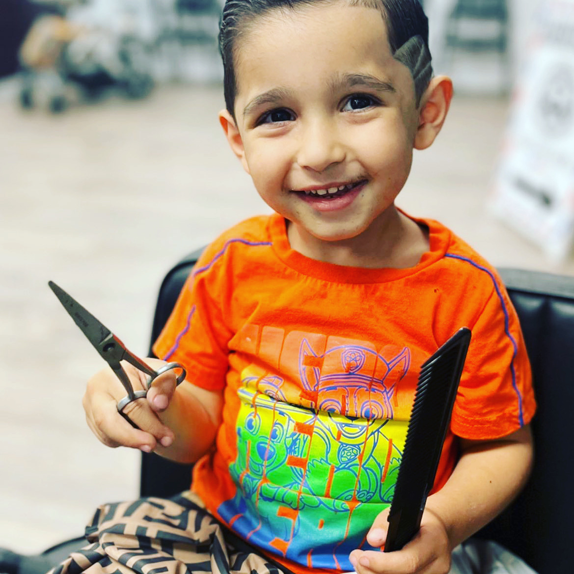 Happy young boy holding barber shears and a comb after his haircut